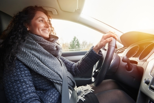 Woman smiling and driving with one hand on steering wheel