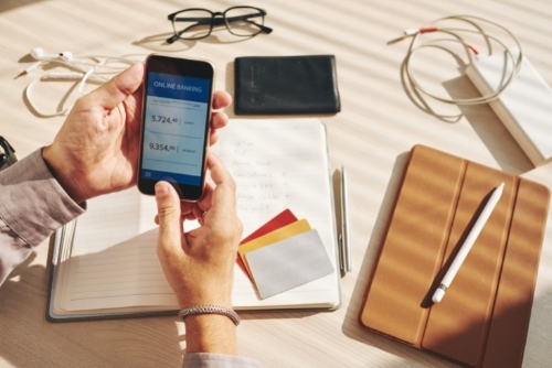 Man sitting at desk looking at bank accounts on cell phone