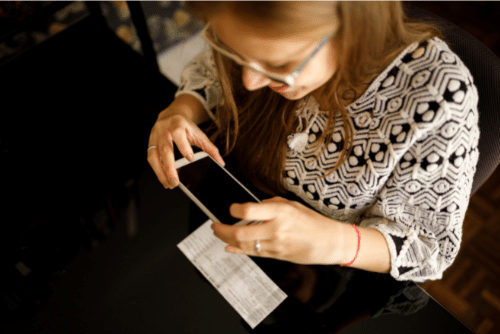 Woman sitting at table taking picture of check with cell phone