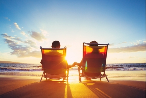 Two people holding hands while sitting on beach at sunset