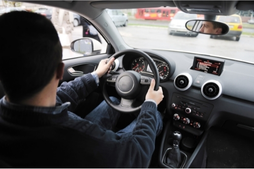 Man driving car with two hands on wheel looking at traffic in parking lot