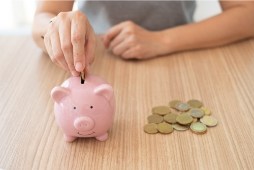 Person placing coins sitting on table into piggy bank