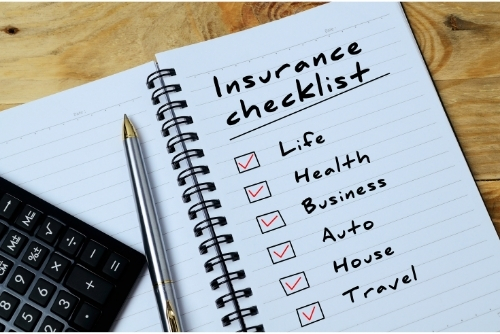 Insurance checklist written on notepad with checkboxes next to Life, Health, Business, Auto, House, and Travel