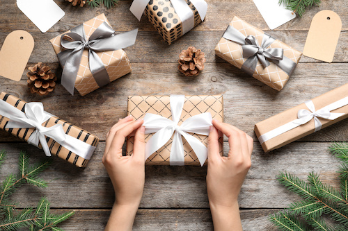 Woman wrapping Christmas gift at wooden table, top view