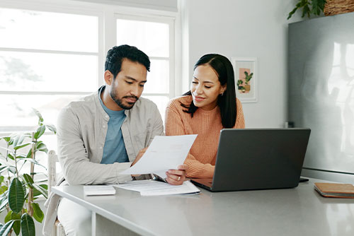 Husband and wife working at kitchen island with paperwork and laptop.